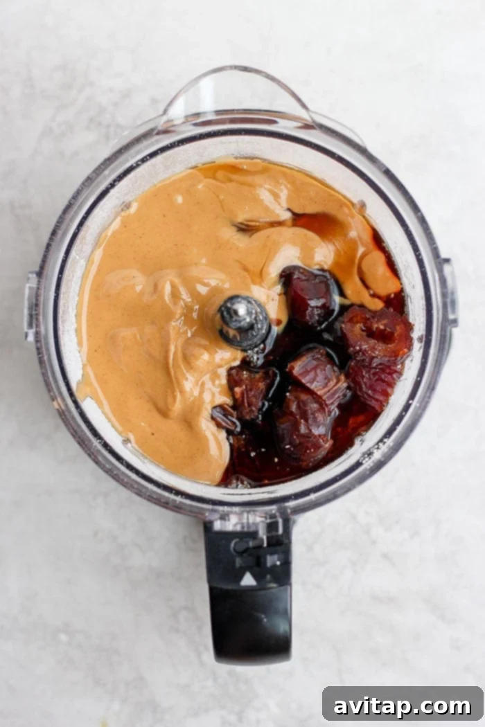 Simple ingredients transform into delicious energy balls with ease. A food processor bowl filled with essential energy ball ingredients like oats, dates, and nuts, poised to be blended into a delicious and healthy snack mixture.