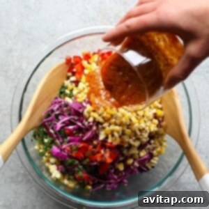 A cook mixing a large bowl of colorful corn salad with a spatula.