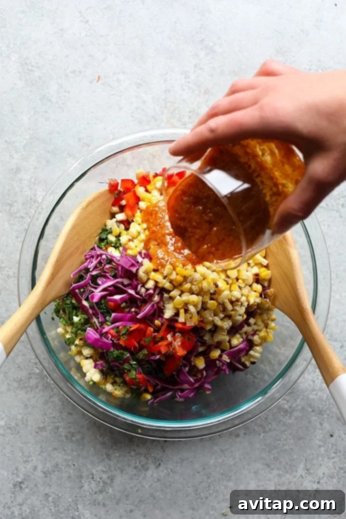 This Thai Chili Summer Corn Salad, featuring grilled corn, carrots, red pepper, cabbage, and a delicious vinaigrette, is a delightful and vibrant dish for any occasion. A colorful medley of corn salad ingredients mixed in a large glass bowl.