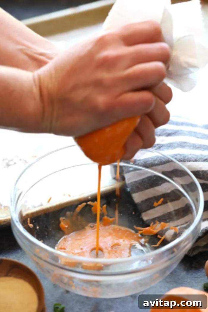 A close-up of hands squeezing liquid out of grated sweet potatoes using a tea towel.