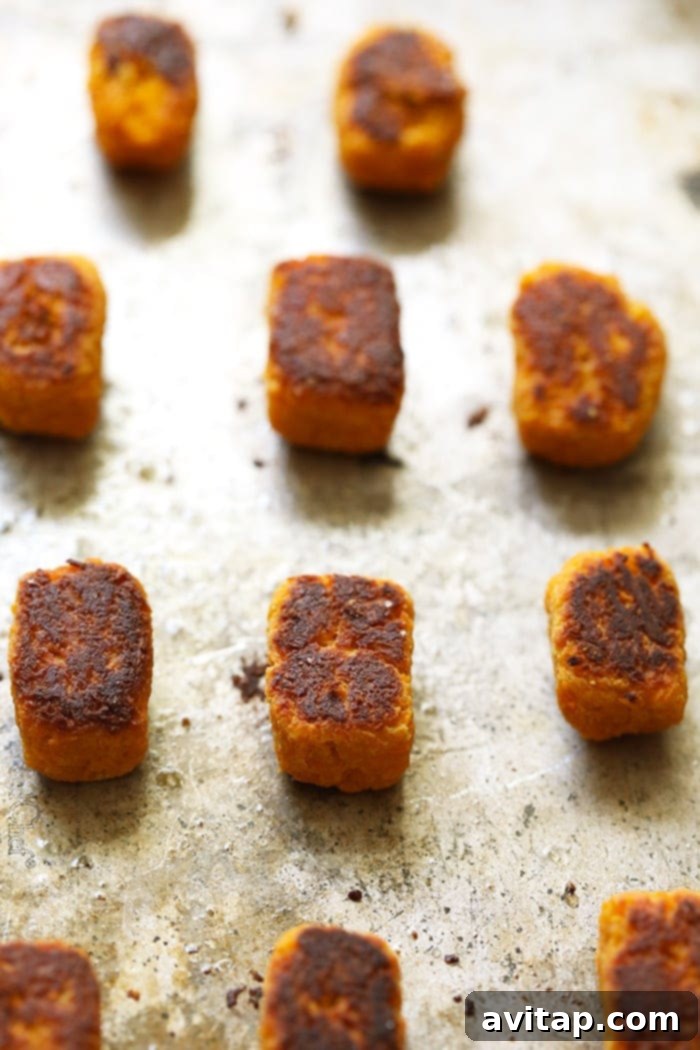 A baking sheet filled with perfectly golden and crispy baked sweet potato tater tots, ready to be served.