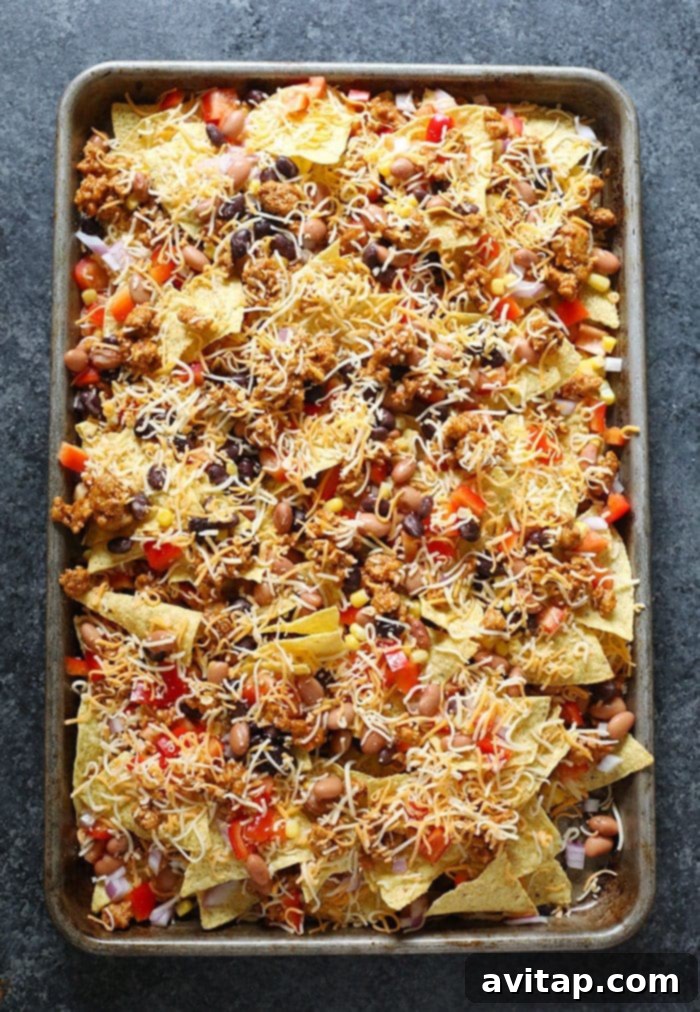 Layered chicken nachos assembled on a baking pan, ready for the oven.