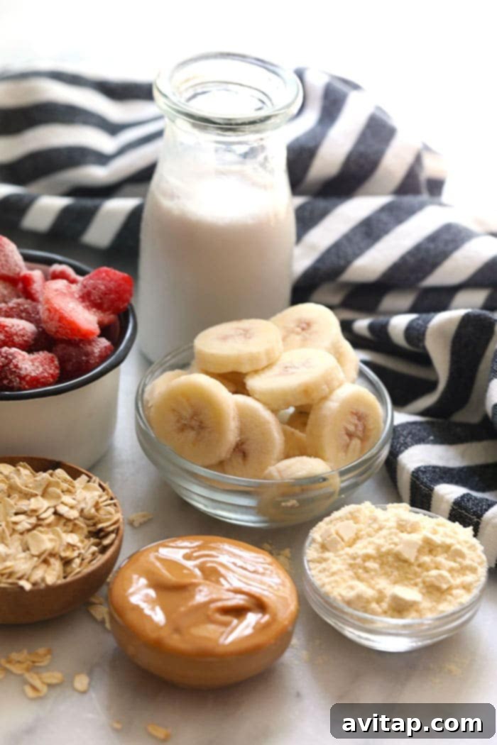 Fresh ingredients ready for blending into a healthy breakfast smoothie. All the healthy breakfast smoothie ingredients laid out: frozen banana, strawberries, oats, protein powder, peanut butter, and almond milk.