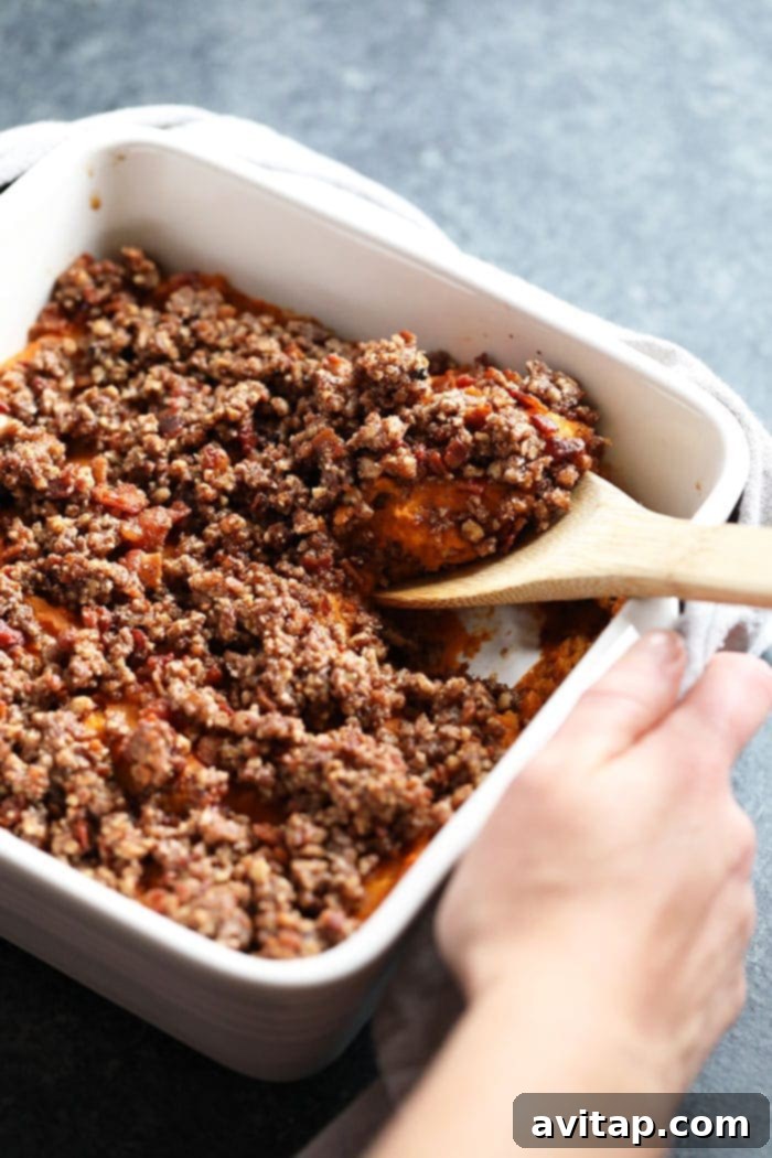 Serve up a healthy sweet potato casserole with a delightful pecan and oat topping this Thanksgiving. Healthy sweet potato casserole being served from a baking dish, showcasing its creamy interior and crunchy topping, ready for a holiday meal.
