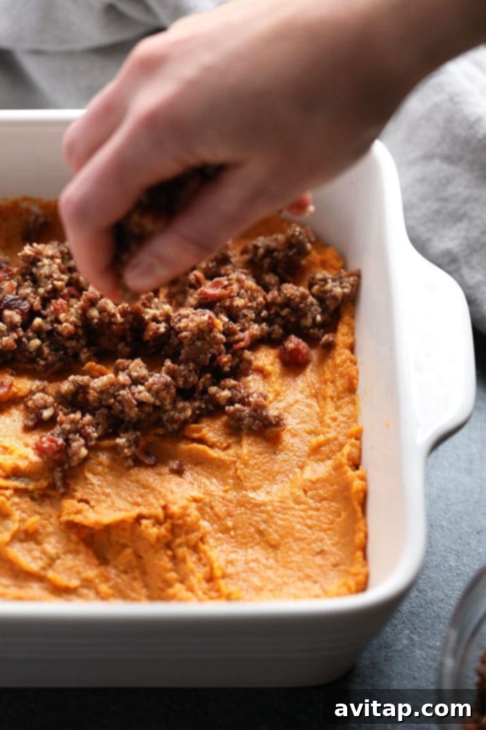 Sprinkle the delicious pecan streusel topping over your creamy sweet potato base before baking for a perfect crunchy finish. Close-up of the delightful crumble topping being sprinkled generously over the creamy pureed sweet potatoes in a baking dish before baking.