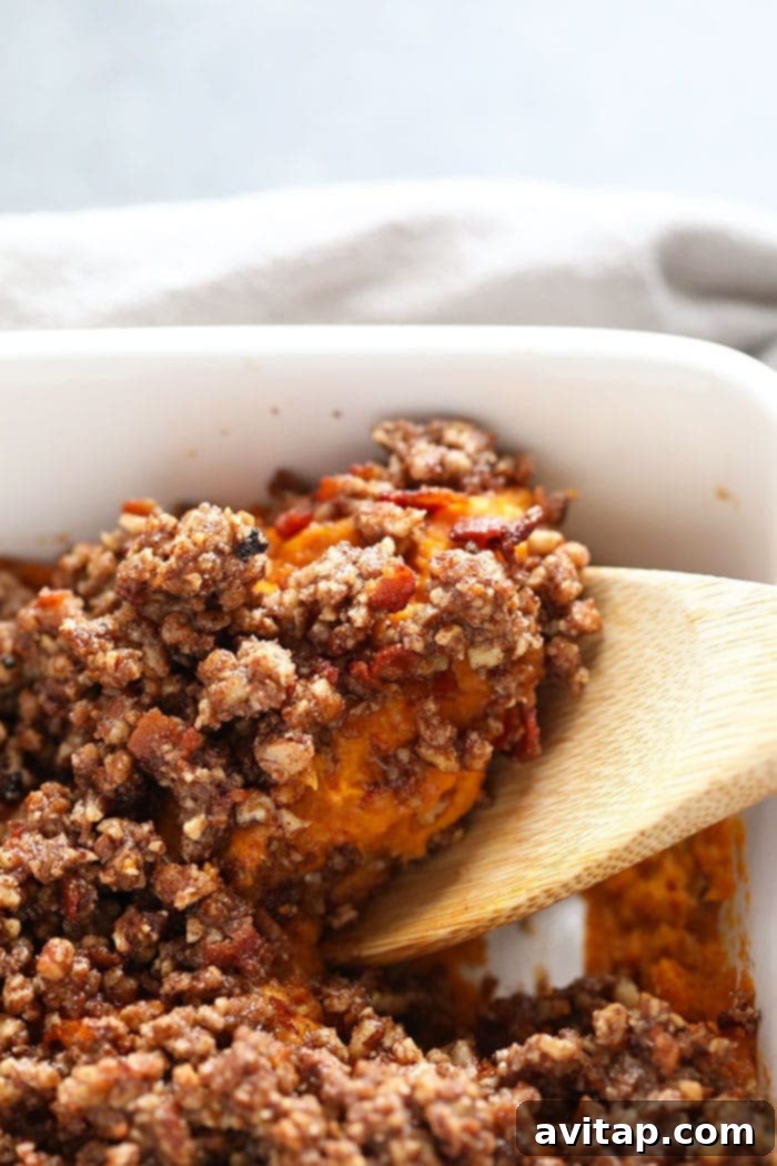 Enjoy a delicious scoop of healthy sweet potato casserole, perfect for any holiday meal and a crowd-pleaser. A serving spoon scooping a generous portion of healthy sweet potato casserole from the baking dish, revealing its rich, creamy texture and crumbly topping.