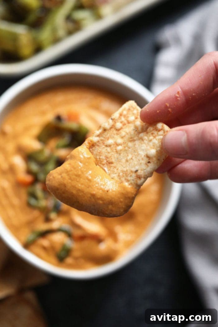 A tortilla chip generously loaded with creamy vegan queso.