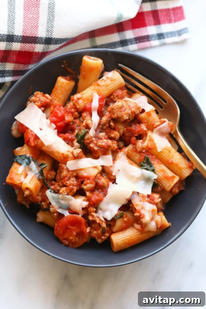 Delicious Sausage Pizza Pasta generously served in a rustic white bowl, garnished with fresh basil leaves.