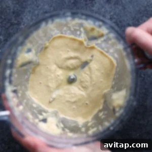 A person blending ingredients for vegan mac and cheese sauce in a blender.