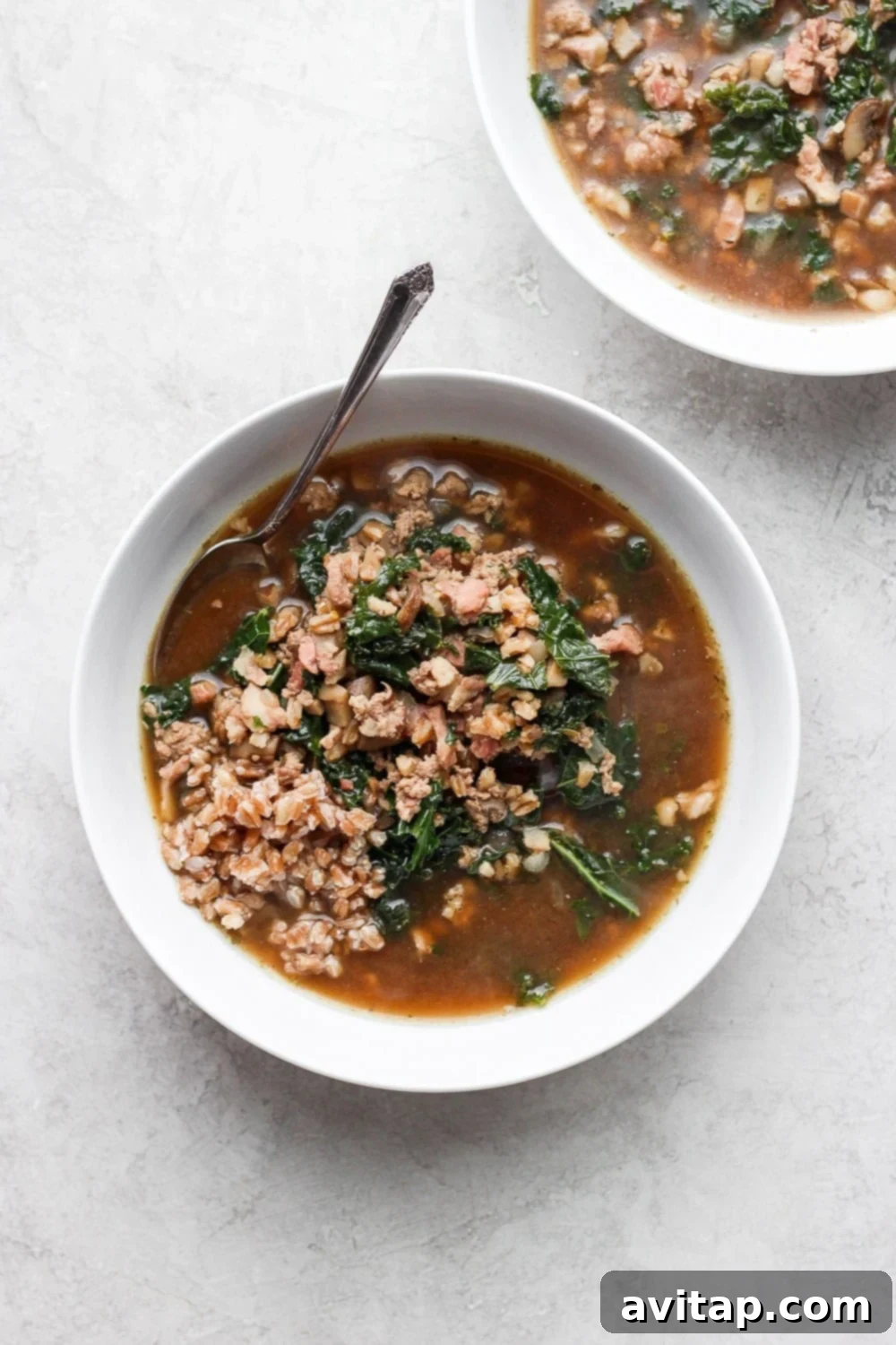 A vibrant bowl of hearty turkey farro soup with fresh kale leaves and a rich broth.