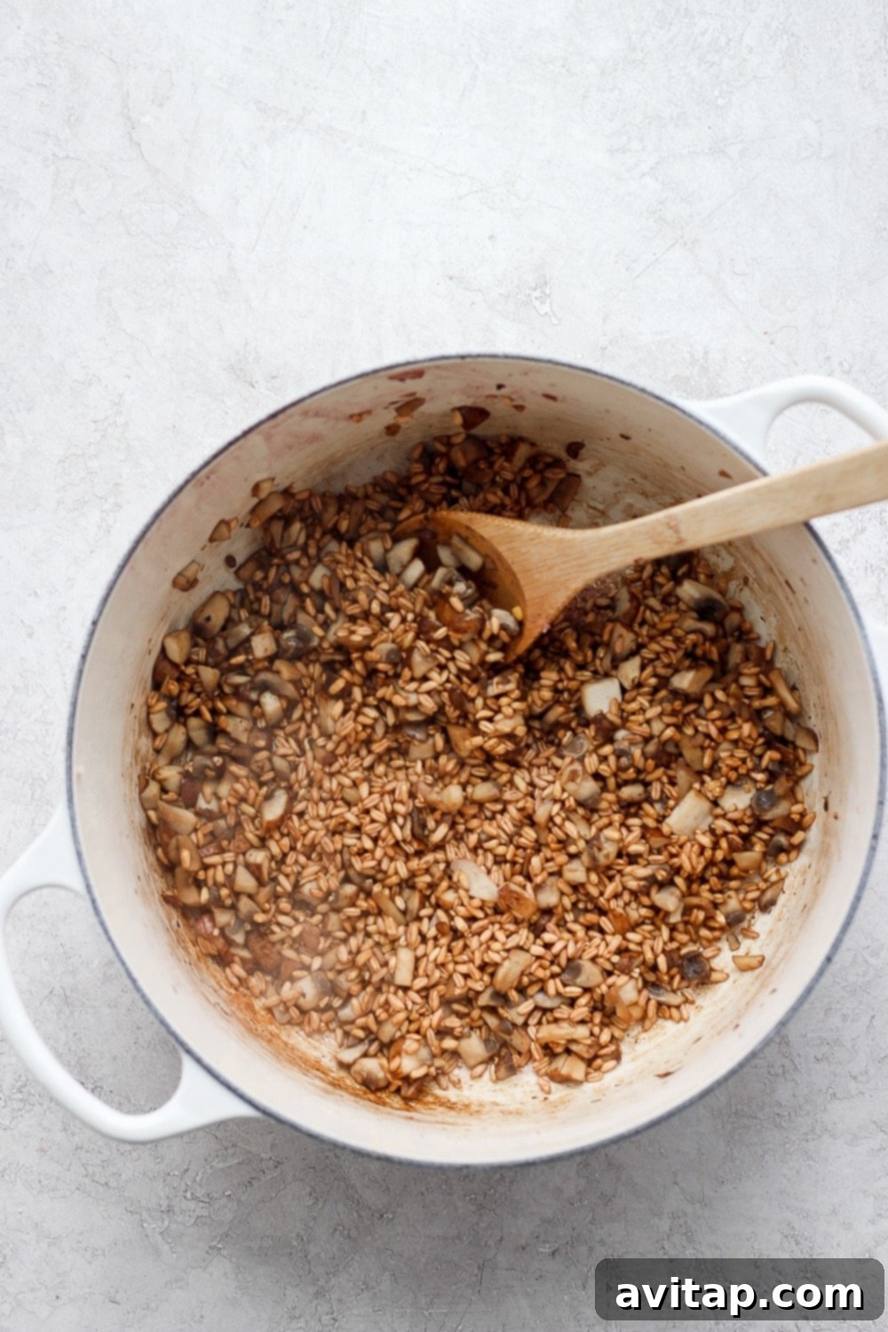Close-up shot of uncooked farro grains being added to a pot with sautéed mushrooms, about to be simmered in broth.