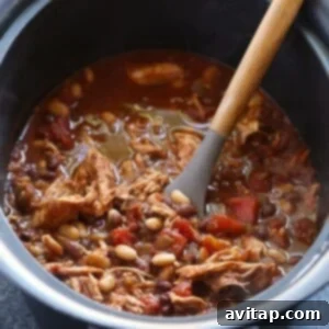 Shredded chicken being stirred into the chili in a crockpot.
