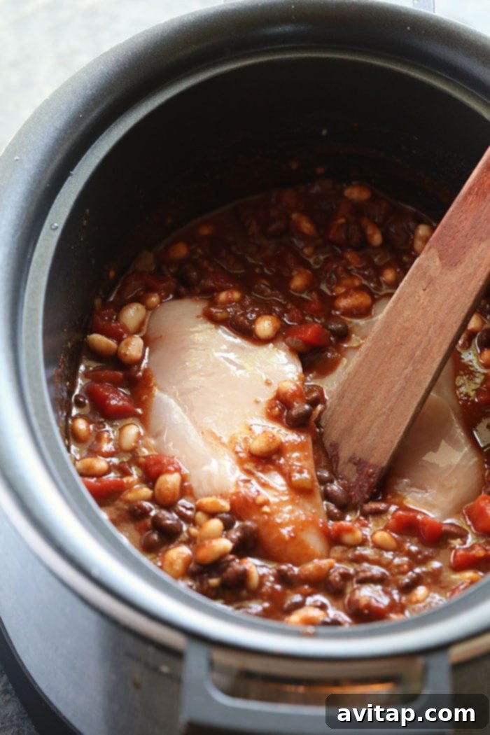 A close-up view of the slow cooker bubbling with delicious chicken chili, showing the texture and rich color.