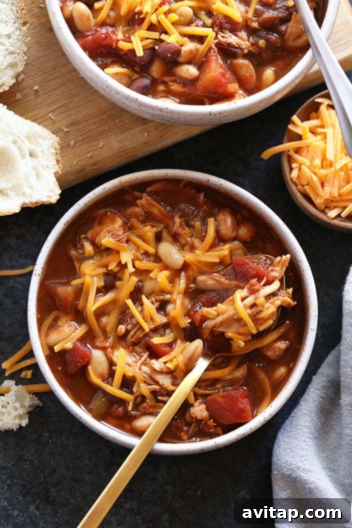 A vibrant bowl of crockpot chicken chili with a variety of toppings like avocado, cilantro, and sour cream.