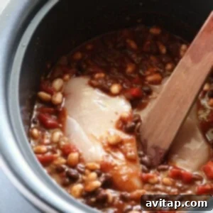A crockpot filled with chili ingredients and chicken breasts, ready to cook.