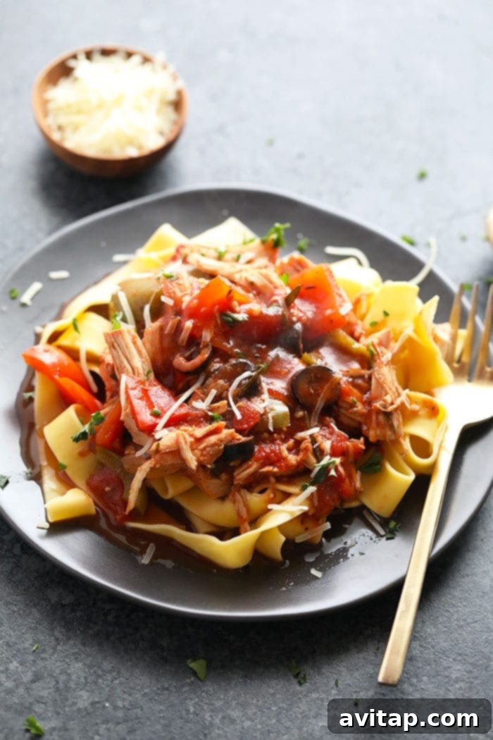 Slow cooker chicken cacciatore generously served over wide pappardelle pasta, garnished with fresh basil and grated Parmesan cheese.