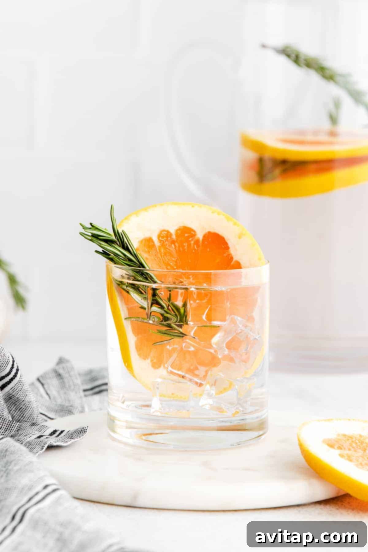 Slices of pink grapefruit and sprigs of fresh rosemary infusing in a glass of water.