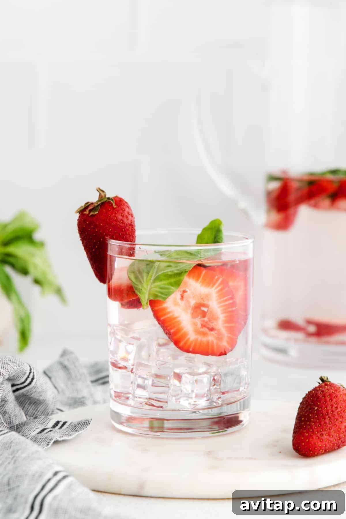 Sliced strawberries and fresh basil leaves infusing in a glass of water.