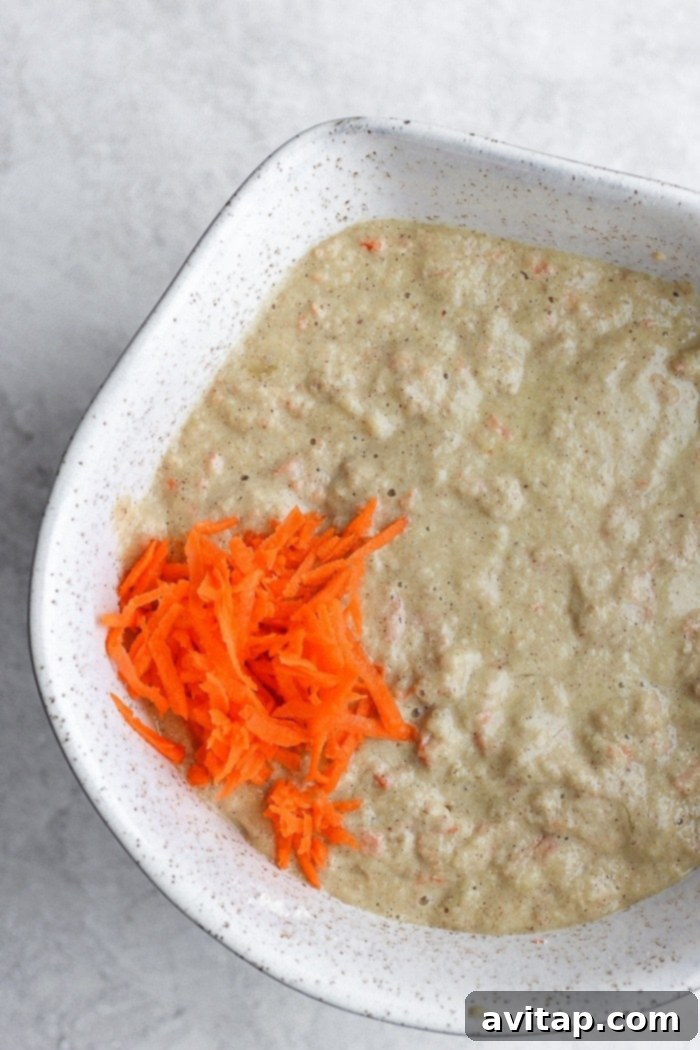 Dry ingredients and shredded carrots mixed in a white bowl, ready for wet ingredients.