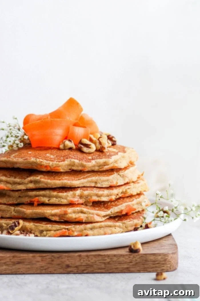 A beautifully arranged stack of healthy carrot cake pancakes, drizzled with syrup and topped with pecans.