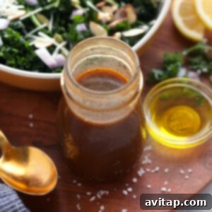 A jar of homemade balsamic vinaigrette next to a fresh kale salad, ready to be served.