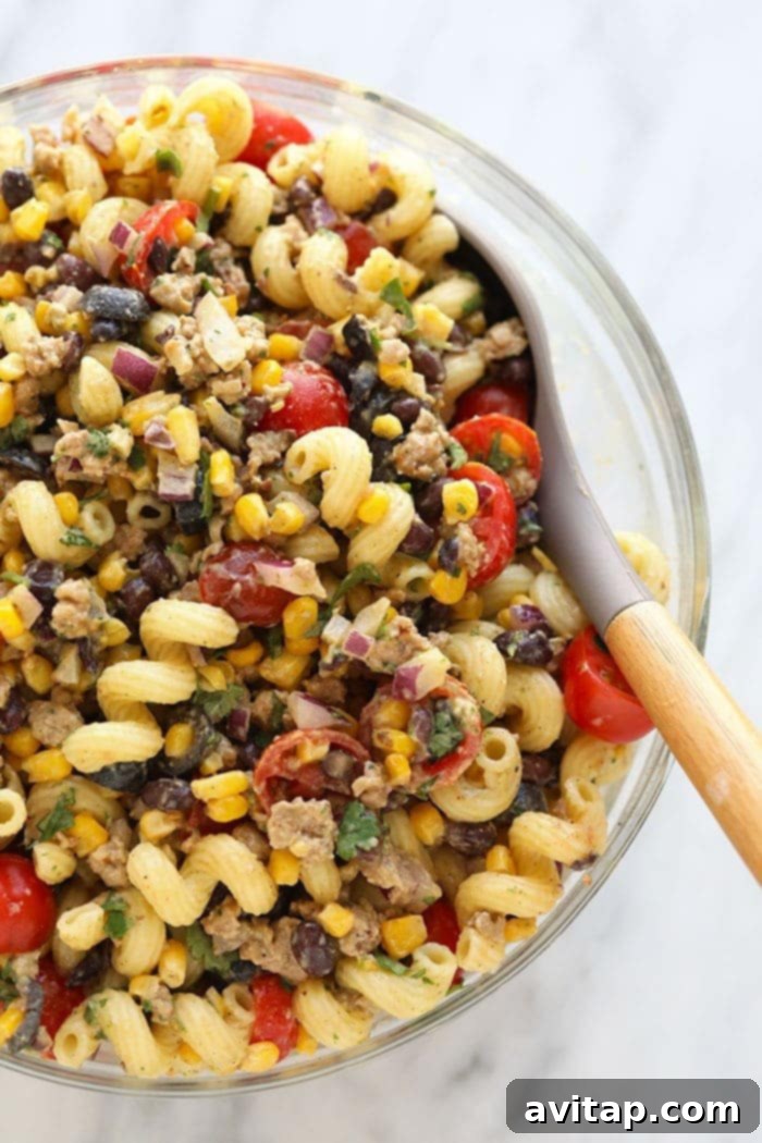 Taco pasta salad in a large, rustic serving bowl, showcasing colorful ingredients like corn, black beans, tomatoes, and seasoned ground meat, garnished with fresh cilantro.
