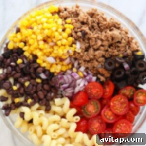 All the vibrant taco pasta salad ingredients, including pasta, seasoned meat, corn, beans, and tomatoes, thoroughly mixed in a large bowl before dressing is added.