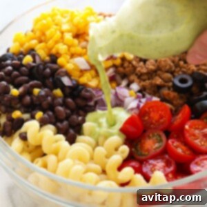 A close-up shot of creamy cilantro lime dressing being poured from a pitcher onto the colorful taco pasta salad, ensuring even coating.