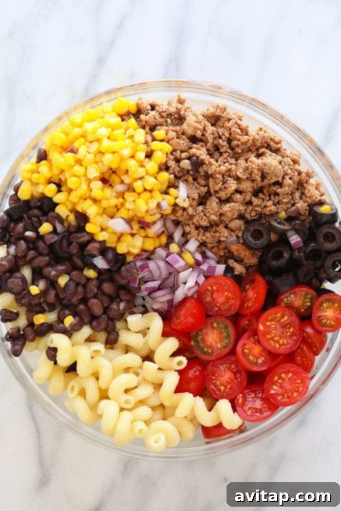 Healthy taco pasta salad elegantly presented in a clear glass bowl, showcasing its fresh ingredients and vibrant colors, ready to be served.