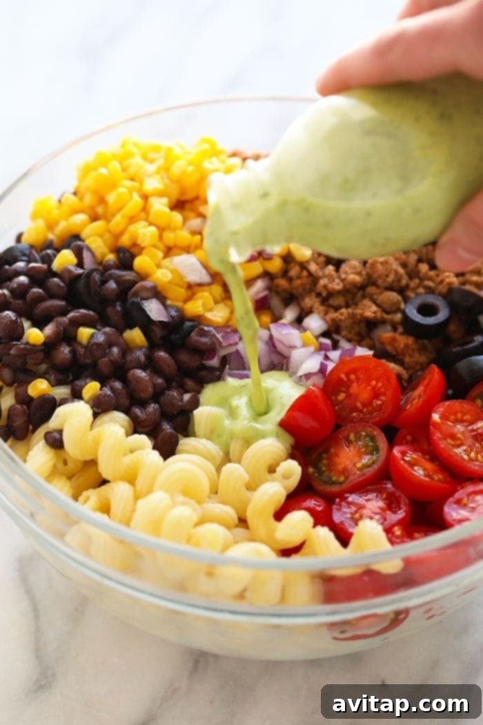 Close-up shot of vibrant, creamy cilantro lime dressing being generously poured over a large bowl of colorful taco pasta salad, ensuring every ingredient is coated.