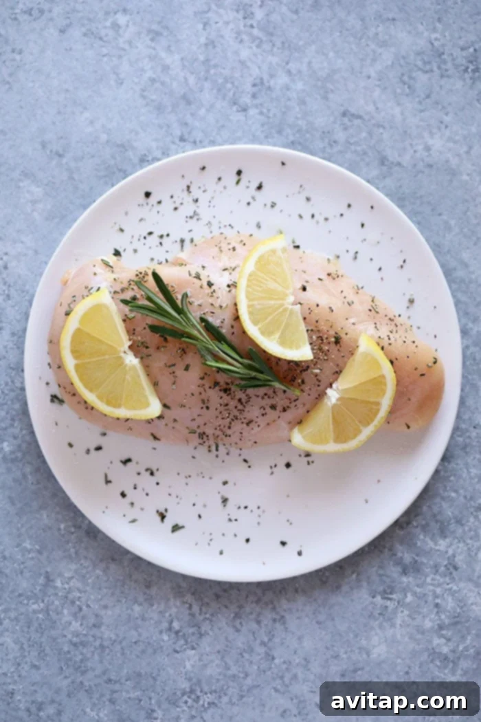Raw chicken breast on a plate with fresh lemons and rosemary sprigs.
