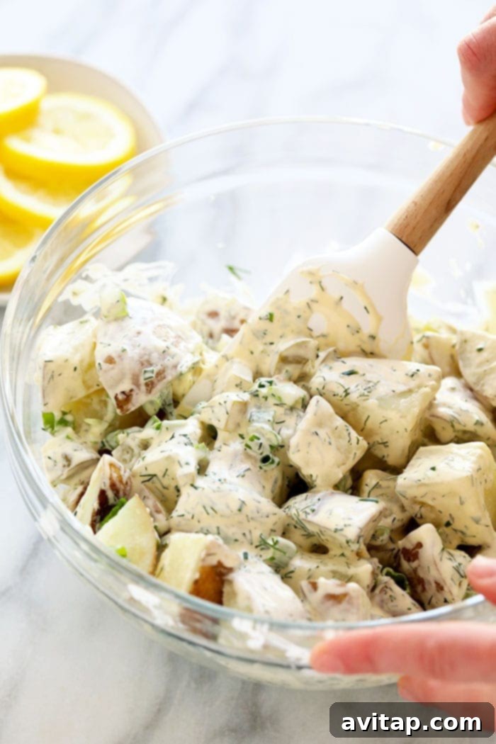 A hand mixing vibrant vegan potato salad in a large bowl, showcasing fresh ingredients.