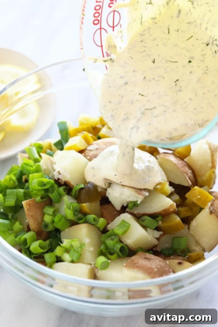 Close-up shot of rich vegan dressing being poured over cooked potato chunks and fresh herbs in a bowl, ready for mixing.