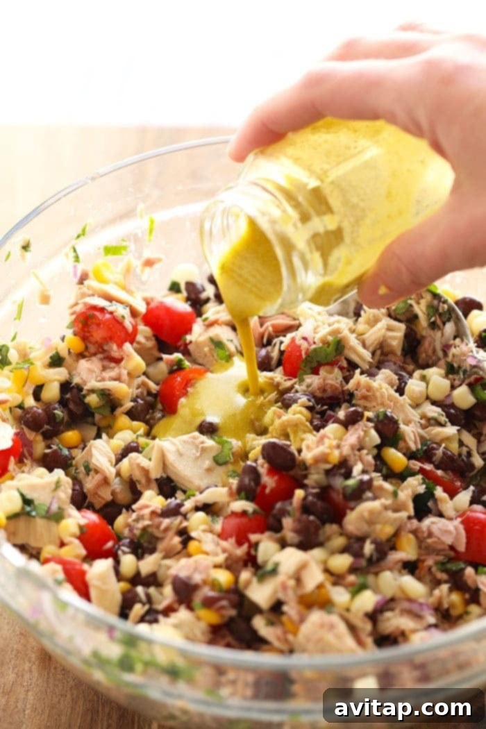 A serving of Fiesta Tuna Salad in a white bowl, highlighting its fresh ingredients and absence of mayo, with a spoon ready for enjoyment.