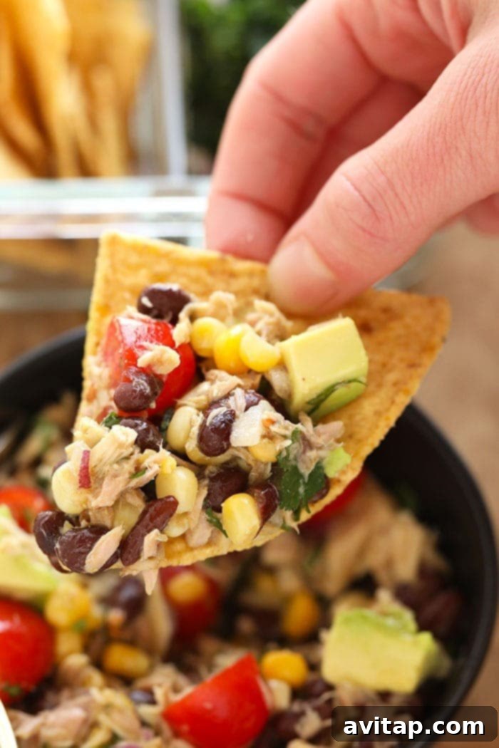 A tortilla chip loaded with colorful Fiesta Tuna Salad, featuring corn, black beans, tomatoes, and cilantro, ready to be eaten.