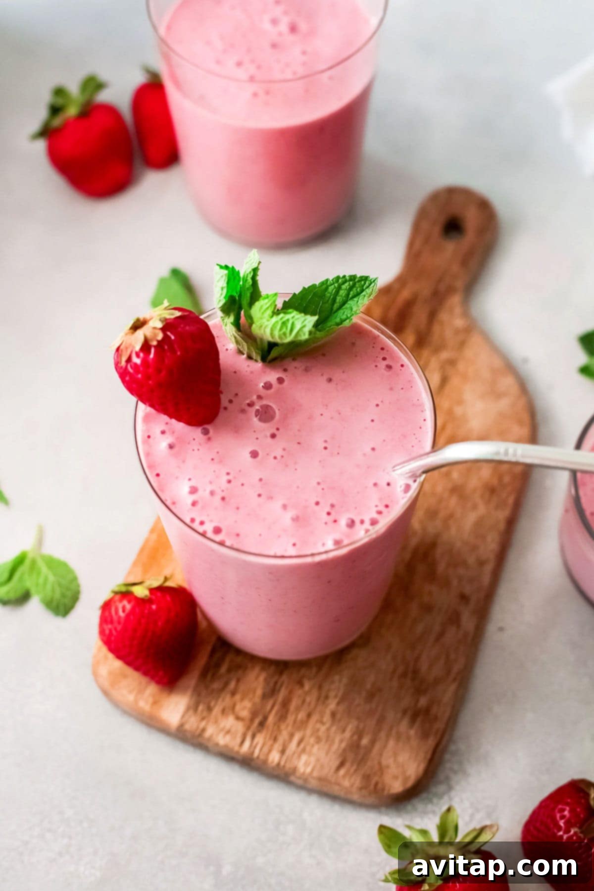 A beautifully blended strawberry banana smoothie in a glass, ready to be enjoyed, with fresh strawberries and banana slices on a wooden cutting board in the background.