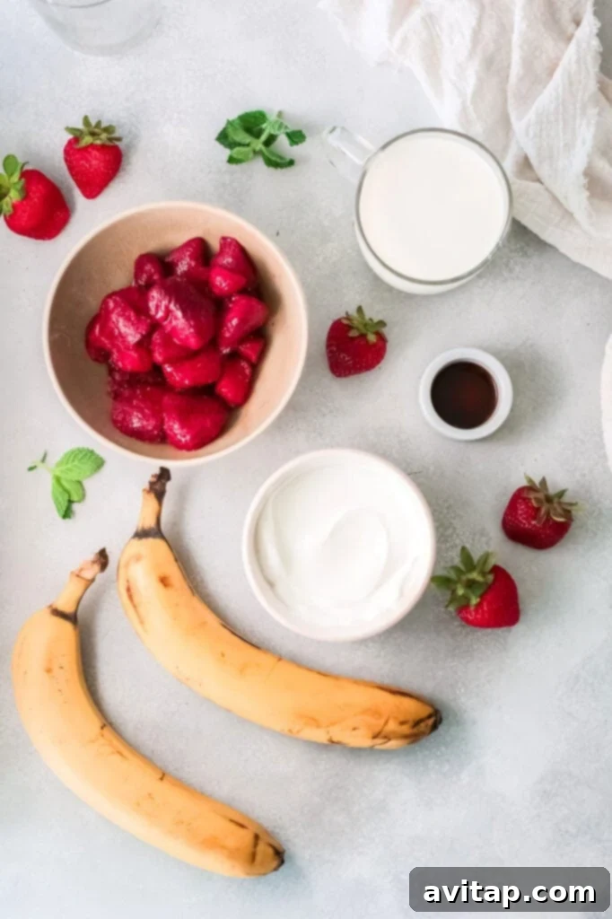 Individual ingredients for a strawberry banana smoothie laid out on a kitchen counter: a bowl of frozen strawberries, sliced frozen bananas, a container of Greek yogurt, a bottle of vanilla extract, and a carton of almond milk.