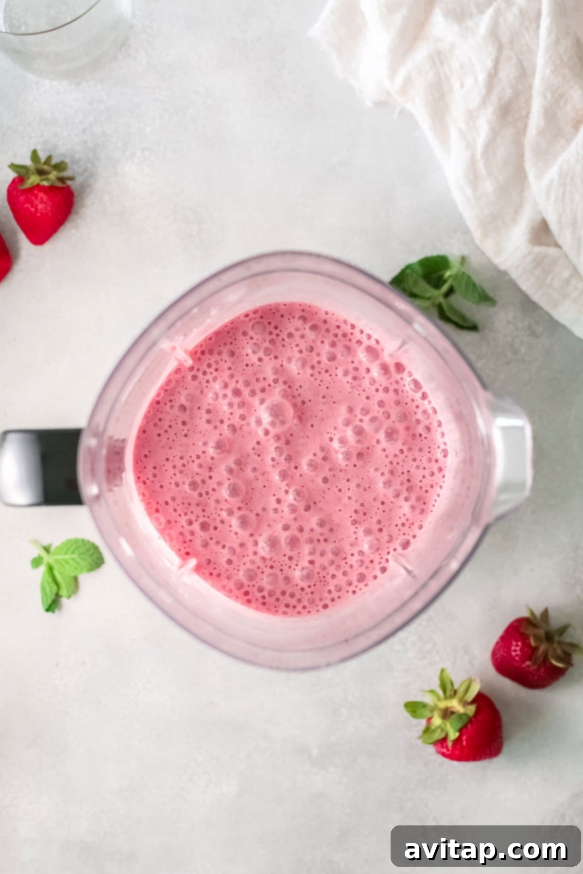 A top-down view of a vibrant strawberry banana smoothie being blended in a high-speed blender, showing the swirling colors and creamy texture.