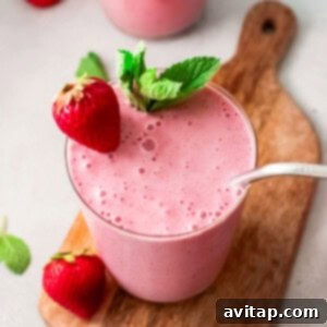 A glass of strawberry banana smoothie with a straw, garnished with a fresh strawberry and banana slices.