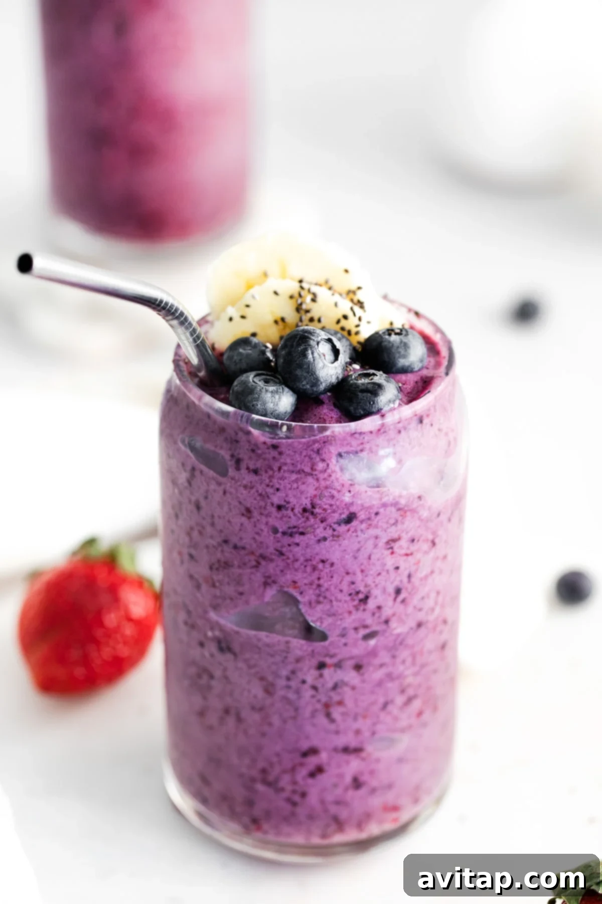 A vibrant triple berry protein smoothie in a glass, garnished with fresh blueberries and chia seeds.