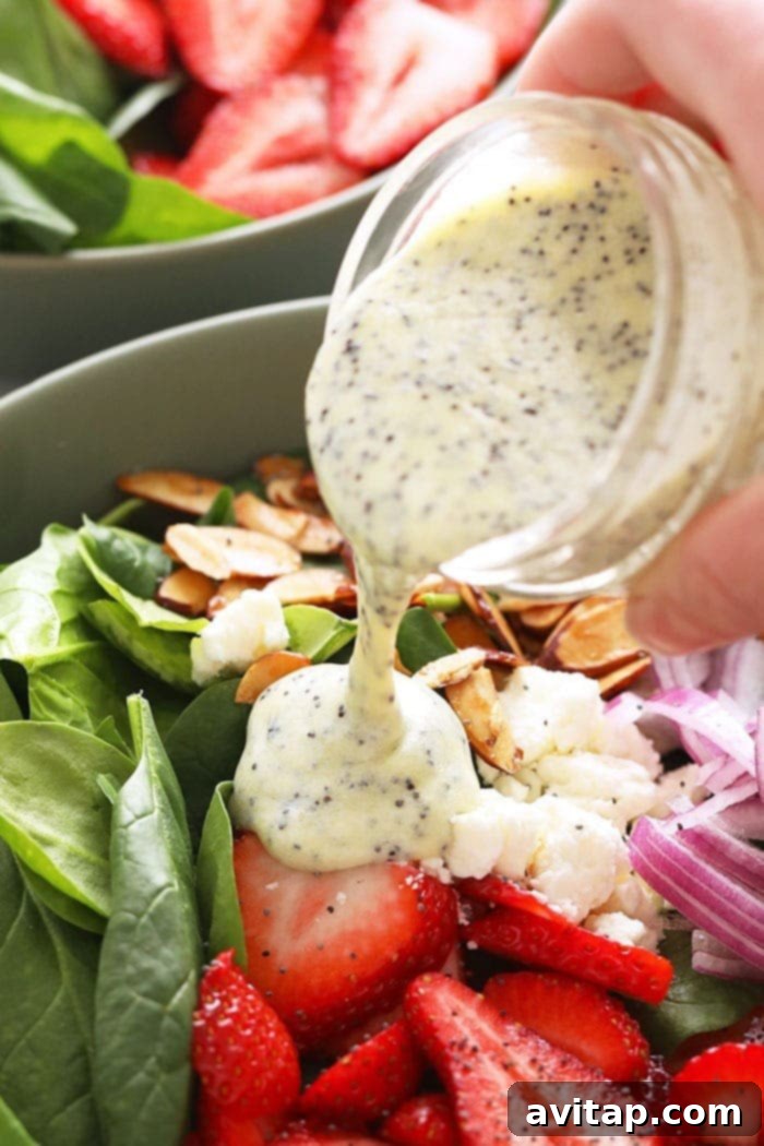 A vibrant salad composed of mixed greens, fresh strawberries, and other vegetables, with a stream of poppy seed dressing being poured over it.