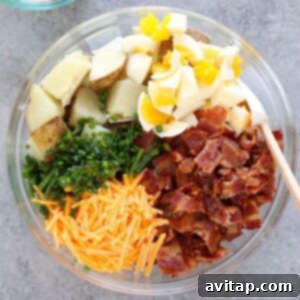 A bowl of baked potato salad with bacon, cheese, and chives.