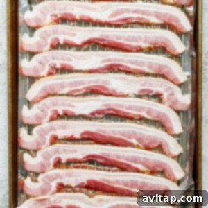 Raw bacon strips neatly laid out in a single layer on a wire rack over a baking sheet.