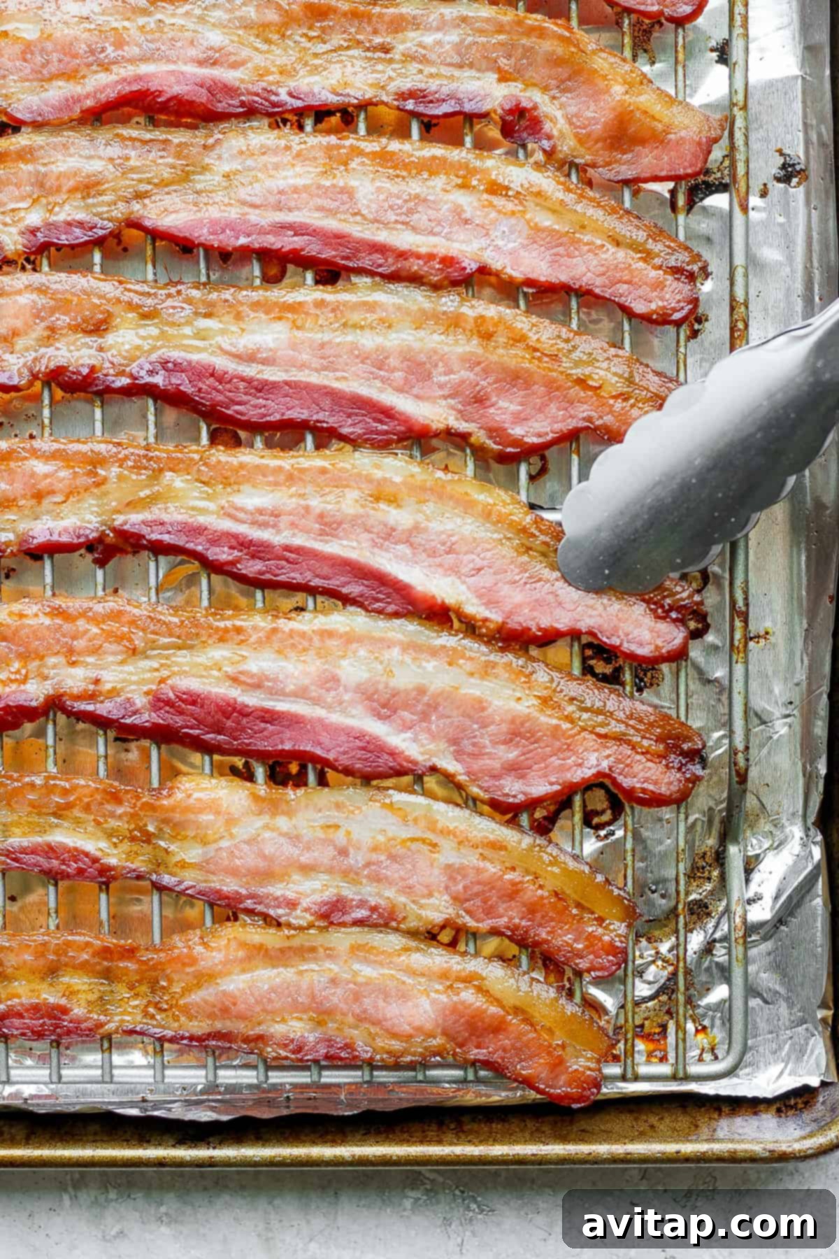 Close-up of golden-brown crispy bacon on a baking sheet, with a fork poised to pick a piece.