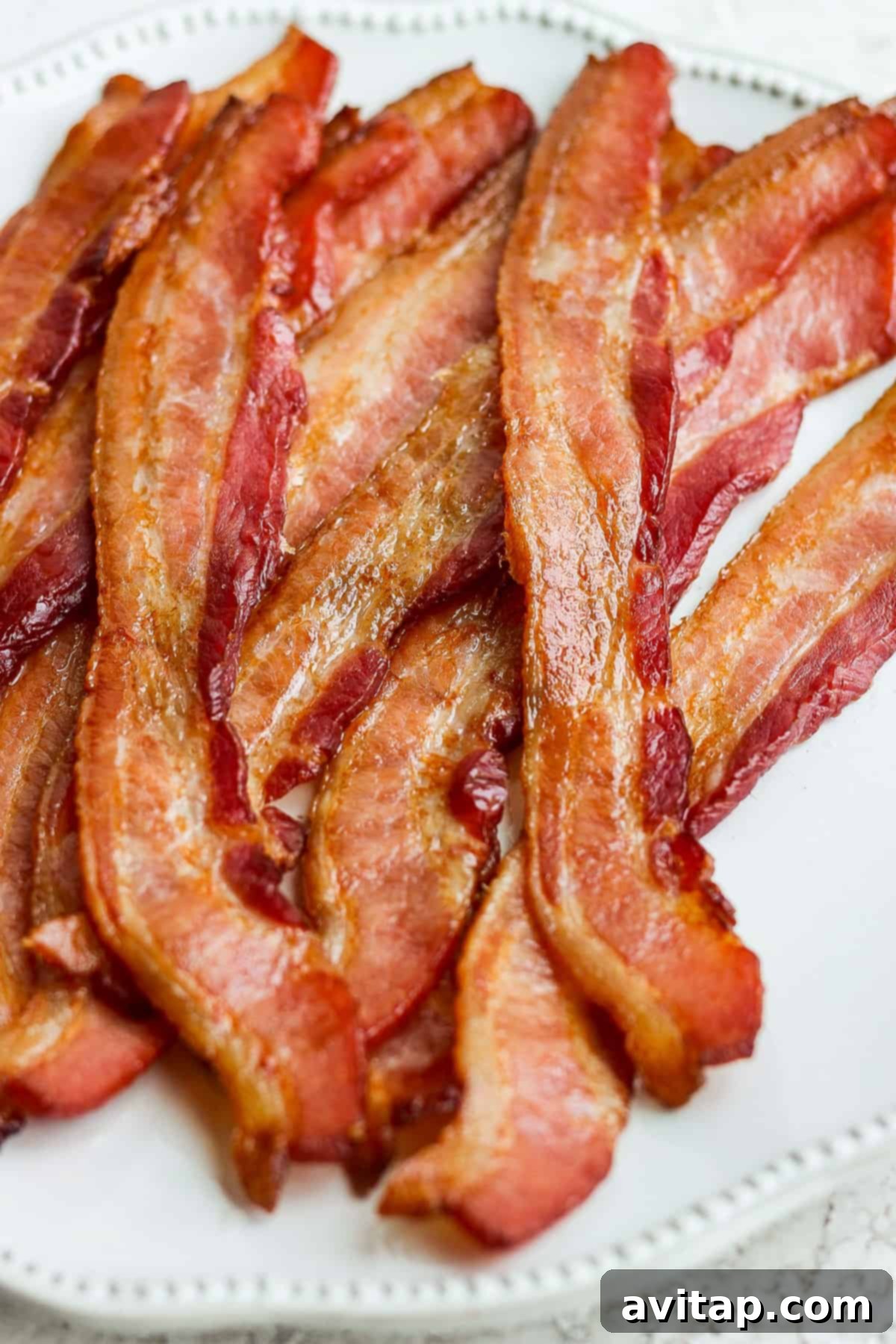 A serving of perfectly oven-baked bacon on a simple white plate, ready to be enjoyed.