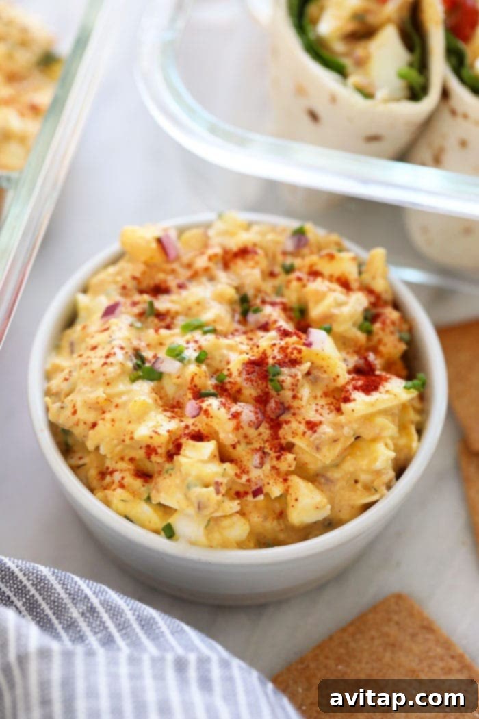 This Tuna Egg Salad blends the flavors you love from tuna salad with egg salad for a satisfying and protein-packed lunch! Filled with a short list of real ingredients, this tuna egg salad recipe can't be beat. Lunch is served! A bowl of tuna egg salad on a wooden table, garnished and ready to serve