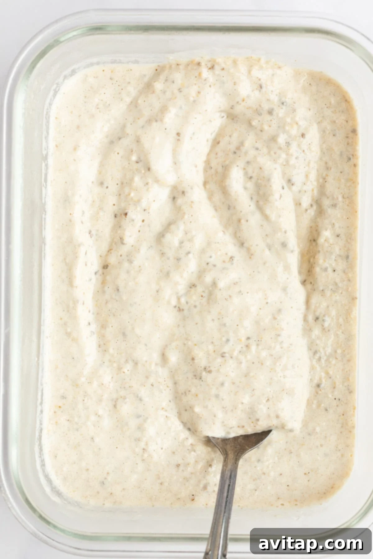 A close-up of a glass jar filled with peanut butter overnight oats, topped with extra peanut butter, a few chocolate chips, and a banana slice.