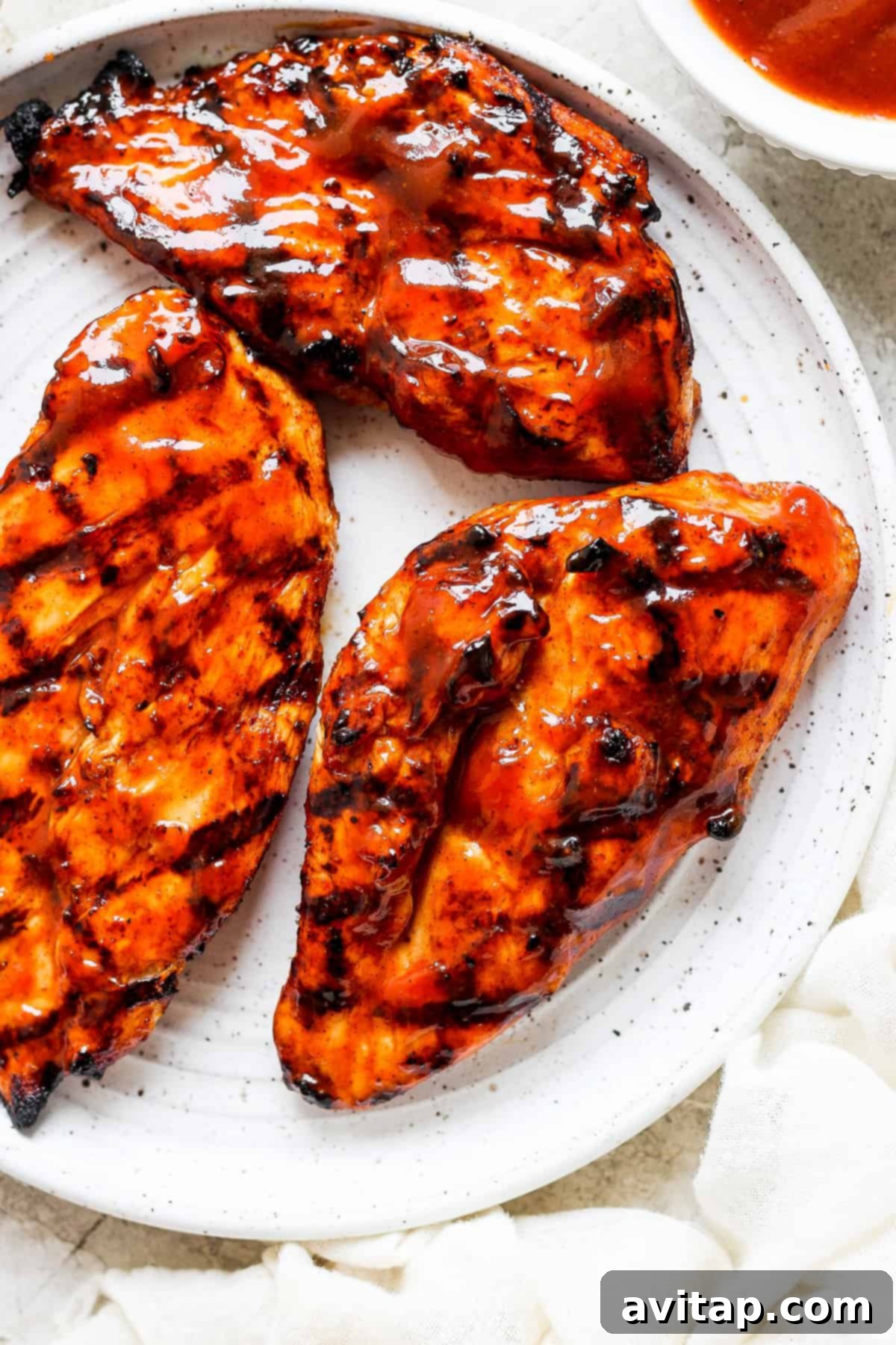 Smoky BBQ Chicken Perfection 2 Grilled chicken breasts on a white plate with sauce and fresh herbs.