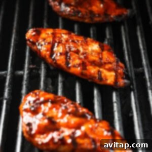 Three grilled chicken breasts on a hot grill with visible flames.