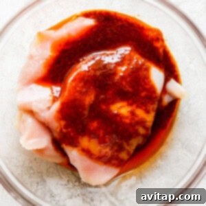 A piece of chicken in a bowl with red marinade.